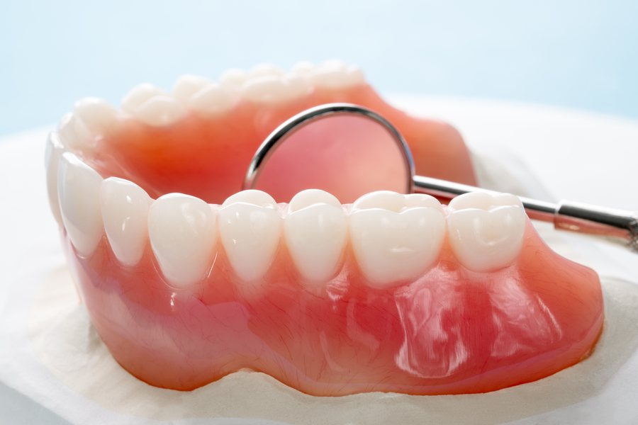 A complete upper and lower denture beside a dental mirror